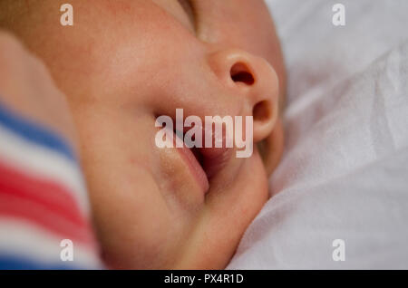 Little baby boy konzentrieren sich auf seinen Mund, schlafen auf weißen quilt Stockfoto