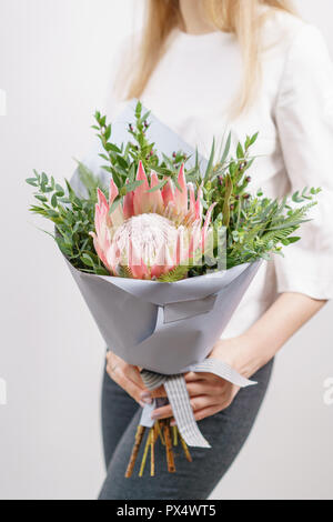 Üppigen Blumenstrauß des Königs Protea, Eukalyptus und andere Grüns. Junge Mädchen, dass eine Blumen Arrangements mit verschiedenen Farben. weiße Wand. Stockfoto