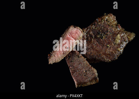 Medium Rindersteak. Mit Pfefferkörnern und Kräutern gewürzt. Auf schwarz isoliert. Bild horizontal mit Kopieren von köstlichen Beefsteak. Stockfoto