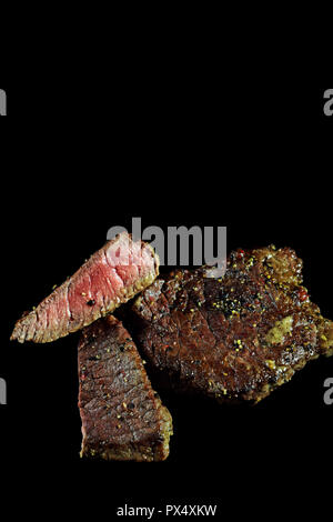 Medium Rindersteak. Mit Pfefferkörnern und Kräutern gewürzt. Auf schwarz isoliert. Bild vertikal mit Kopieren von köstlichen Beefsteak. Stockfoto