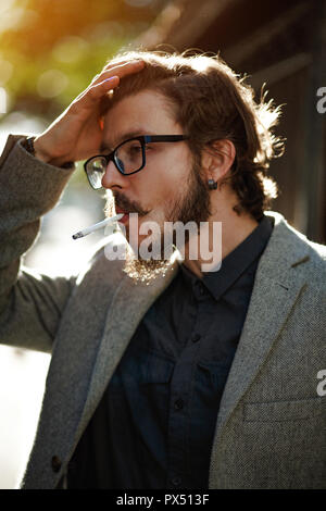 Ein Mann mit langen Haaren raucht außerhalb Stockfoto