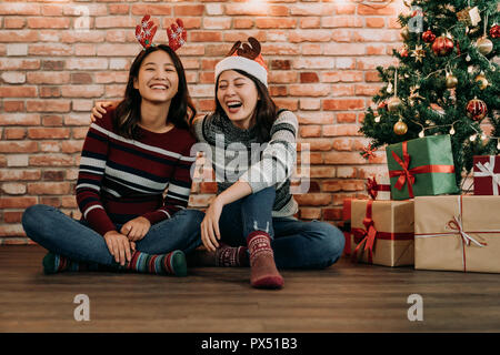 Jugendliche fröhlich sitzen auf dem Holzboden. Junge Mädchen Freunden Spaß zu Hause. Heiligabend indoor Konzept feiern. Stockfoto