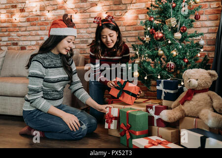 Teenager mit Freude zu Hause für Heiligabend vorbereitet eingerichtet. jungen Schwestern Geschenke unter dem Weihnachtsbaum. wunderbares Team arbeiten, für kommende neue Stockfoto