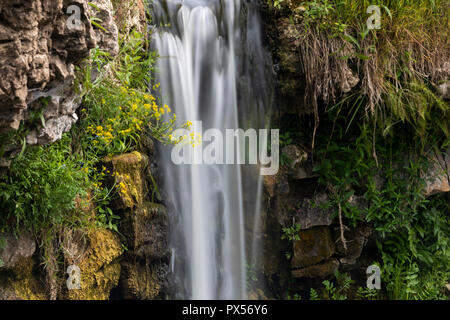 Ein kleiner Wasserfall über Steine mit Moos und Gras fallen Stockfoto