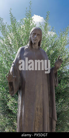 Bronze Skulptur von Jesus Christus. Der Erlöser seine Arme geöffnet hat, Er trägt eine Tunika. Grüne Pflanze im Hintergrund. Stockfoto