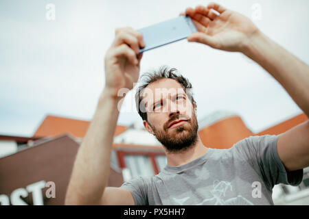 Junger bärtiger Mann Fotografieren einer Skyline der Stadt mit seinem Smartphone Stockfoto
