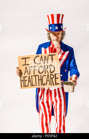 Eine unle SAM-Figur mit einem Schild, auf dem "Ich healthcare nicht leisten' und posieren, als ob er Betteln vor. Stockfoto