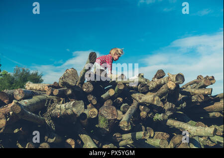 Ein kleines Kind klettern auf einige Protokolle im Wald Stockfoto