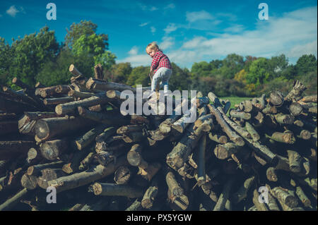 Ein kleines Kind klettern auf einige Protokolle im Wald Stockfoto