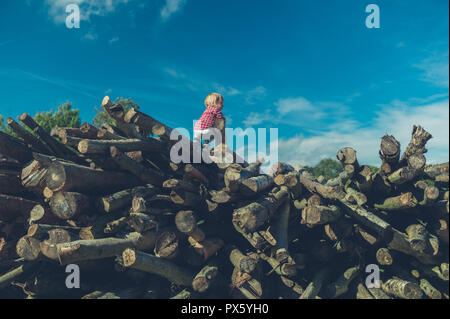 Ein kleines Kind klettern auf einige Protokolle im Wald Stockfoto