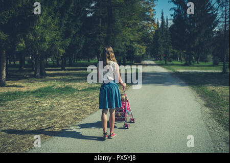 Eine junge Frau wird zu Fuß in einem Park mit einem Kleinkind im Kinderwagen Stockfoto