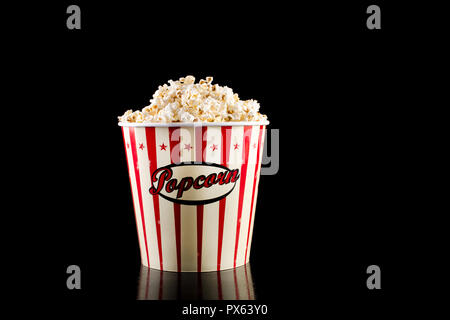 Retro popcorn Box in Rot und Weiß und voll mit Popcorn auf schwarzem Hintergrund im Studio isoliert. Film und Kino essen Konzept Stockfoto