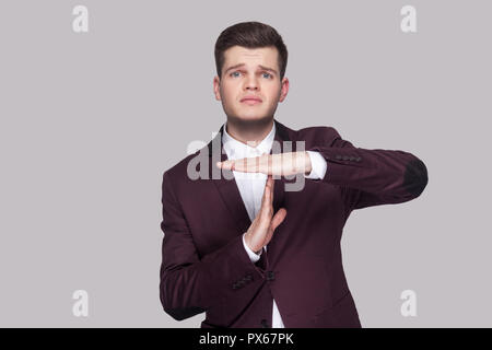 Portrait von Sorge plädieren hübscher junger Mann in violett Anzug und weißes Hemd, stehen, zu Kamera suchen und anzeigen timeout Geste unterzeichnen. indoor Stu Stockfoto