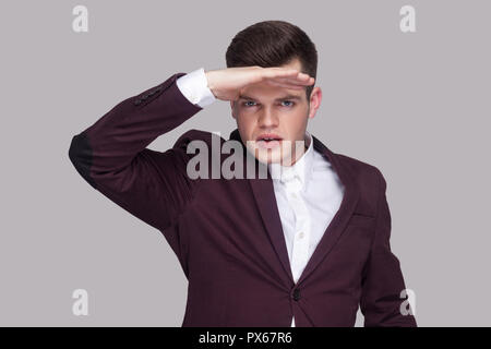 Portrait von Stattlichen ernsthaften jungen Mann in violett Anzug und weißes Hemd, stehen, schauen fern und halten die Hand auf seine Stirn. indoor Studio shot, iso Stockfoto