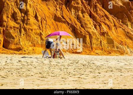 29. September 2018 Ein paar sitzen im Schatten der Sonne brolly auf einem entfernten Teil der Faleisia Strand an der Algarve in Portugal Stockfoto