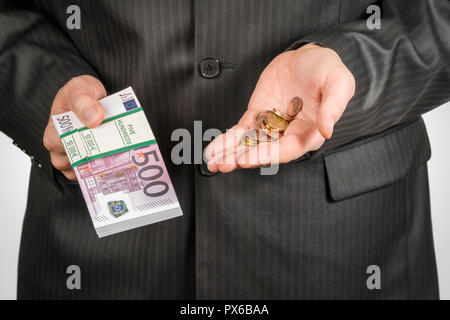 Mann im Anzug hält in einer Hand ein Bündel Geld in Stückelungen von 500 Euro und in der anderen Hand eine Handvoll Münzen. Stockfoto