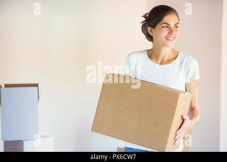 Eine schöne junge Frau trägt einen Karton, der nach dem Einzug in Ihr neues Zuhause Stockfoto