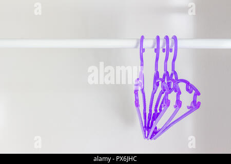 Kleiderbügel aus Kunststoff hängen auf der Schiene. Stockfoto
