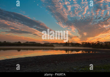 In rot, rosa und gelbe Wolken bei Sonnenaufgang hervorgehoben, ihre Reflexion im Wasser und feinen Nebel. Schöne, mystische, Oktober Morgen am See. P Stockfoto