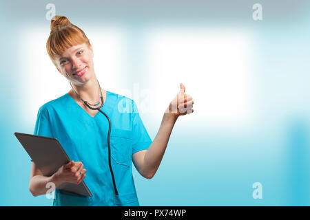Schönen Frau, eine Krankenschwester oder der Arzt mit roten Haaren, mit Daumen nach oben posiert während eines Tablet-PC Stockfoto