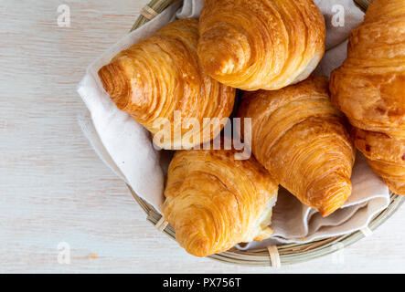 Butter Croissants in kleinen Weidenkorb. Antenne (oben) Blick auf klare Holz Hintergrund. Stockfoto