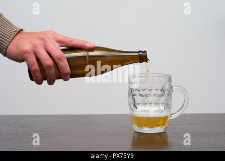 Ein Pint Blondes Bier aus der Flasche füllen, Ale oder Lager von Hand in eine Tankard gießen Stockfoto