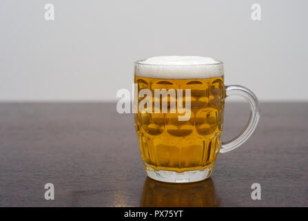 Bier in einem dimplierten Pint Glas auf einem dunklen Holztisch, einem Tankard von Blond Lager oder Pilsner Stockfoto