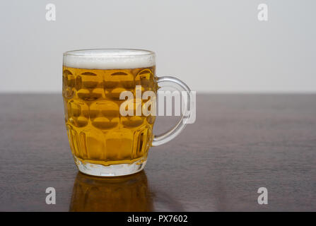 Bier in einem dimplierten Pint Glas auf einem dunklen Holztisch, einem Tankard von Blond Lager oder Pilsner Stockfoto