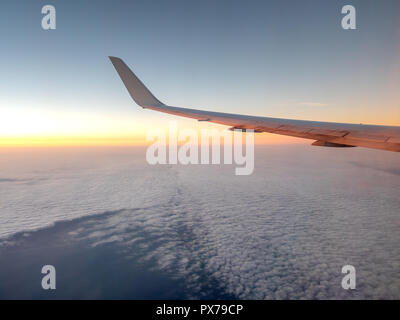 Sunrise Casting orange Tönen auf den linken Flügel der Flugzeug in großer Höhe Stockfoto