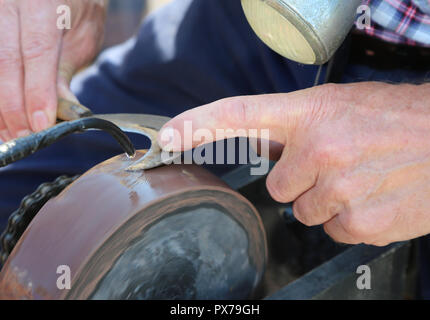 Die Hand eines alten Mannes schleift während seine Messer knoterhaken Blade auf einer alten drehende Mühlstein mit den Tropfen Wasser Abkühlen schärfen Stockfoto