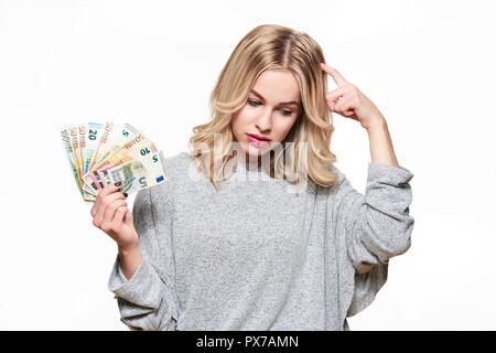 Hübsche, junge Frau im grauen pullover Holding Bündel von Euro-banknoten, ihr Kopf denken, auf weißem Hintergrund zu kratzen. Stockfoto