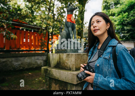 Asiatische Fotograf steht vor dem Hund Statue und in den Himmel schauend. Junge Mädchen Hobby Fotografieren von slr-kamera. religion Travel Tourist i Stockfoto