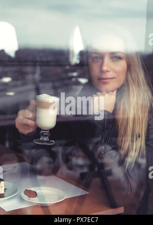 Porträt einer Frau mit Tasse Milchkaffee im Café saßen und draussen durch die Fenster, die Ruhe und Entspannung Konzept Stockfoto