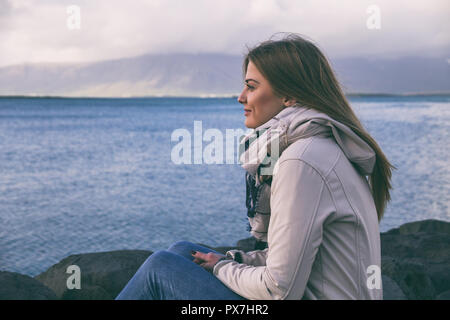 Schöne Frau genießt durch das Meer in Reykjavik sitzen. Image enthält wenig Lärm wegen der hohen ISO auf Kamera eingestellt und es getönt. Stockfoto