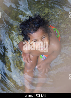 Ein junges Mädchen in einem Fluss sitzend in die Kamera lächeln, Thailand Stockfoto