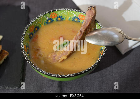 Rote Linsensuppe mit geräuchertem Rippchen in einem hellen Grün Schüssel mit floralen Ornament. Dunkelgrau Stoff Hintergrund. Stockfoto