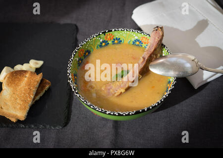 Rote Linsensuppe mit geräuchertem Rippchen in einem hellen Grün Schüssel mit floralen Ornament. Dunkelgrau Stoff Hintergrund. Stockfoto