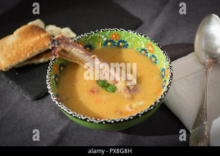 Rote Linsensuppe mit geräuchertem Rippchen in einem hellen Grün Schüssel mit floralen Ornament. Dunkelgrau Stoff Hintergrund. Stockfoto