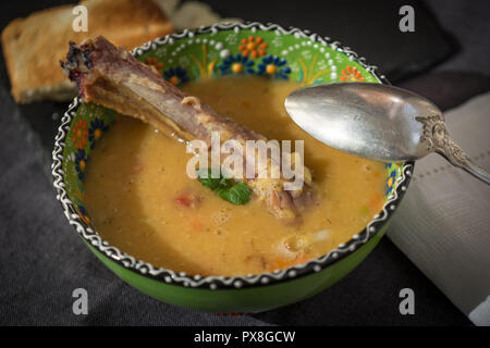 Rote Linsensuppe mit geräuchertem Rippchen in einem hellen Grün Schüssel mit floralen Ornament. Dunkelgrau Stoff Hintergrund. Stockfoto