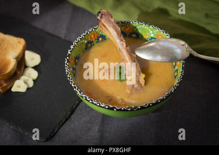 Rote Linsensuppe mit geräuchertem Rippchen in einem hellen Grün Schüssel mit floralen Ornament. Dunkelgrau Stoff Hintergrund. Stockfoto