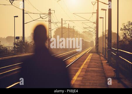 Silhouette der Mann am Bahnhof Plattform bei Sonnenaufgang warten. Stockfoto