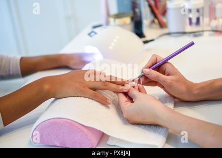 Close-up Kosmetikerin Malerei Nägel eine Frau mit einem Pinsel in ein Nagelstudio. Kunden erhalten eine Maniküre. Stockfoto