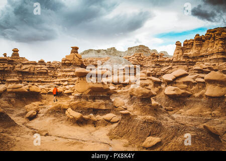 Panoramablick auf Wanderer in rote Jacke in Goblin Valley State Park inmitten wunderschöner hoodoos Sandsteinformationen, Utah, USA Stockfoto