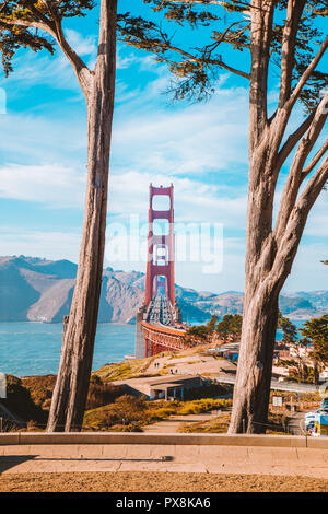 Klassische Ansicht der berühmten Golden Gate Bridge von alten Zypressen bei Scenic Presidio Park gerahmt an einem schönen sonnigen Tag mit blauen Himmel und Wolken, San F Stockfoto