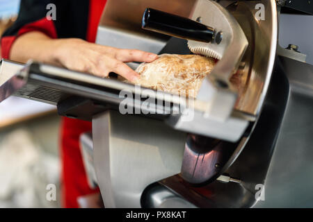 In der Nähe der weiblichen Metzger schneiden York Schinken in eine Schneidemaschine in einer Metzgerei. Stockfoto