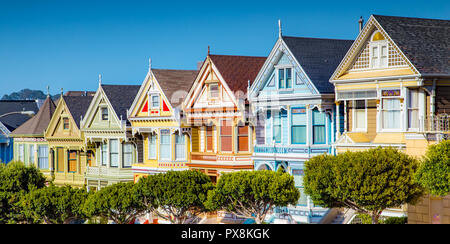 Klassische Postkarte Ansicht des berühmten gemalten Damen, eine Reihe von bunten Viktorianischen Häusern, in der Nähe von malerischen Alamo Square entfernt, an einem sonnigen Tag mit Blu Stockfoto