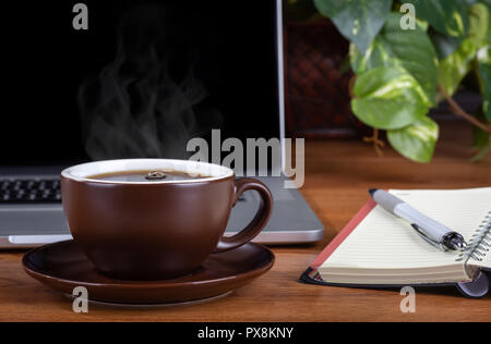 Nahaufnahme einer dampfenden Tasse Kaffee auf einem Desktop-PC zu einem Notebook und Laptop im Hintergrund Stockfoto