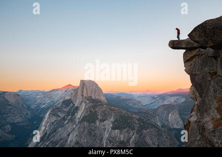 Eine furchtlose Wanderer steht auf einem überhängenden Felsen genießen den Blick auf die berühmten Half Dome am Glacier Point in schönen Abend dämmerung Blicken Stockfoto