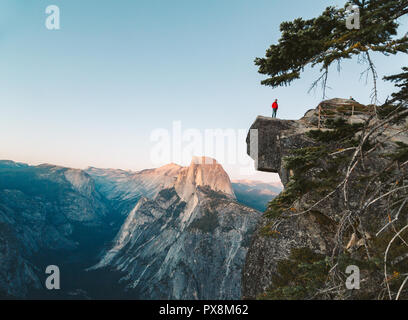 Eine furchtlose Wanderer steht auf einem überhängenden Felsen genießen den Blick auf die berühmten Half Dome am Glacier Point in schönen Abend dämmerung Blicken Stockfoto