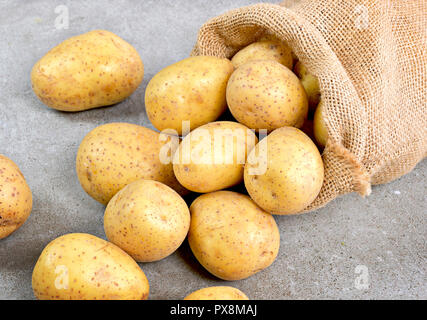 Frische rohe Kartoffeln in einem sackleinen Sack. Erdige Kartoffel Szene mit Sack, Anordnung auf einer hölzernen Hintergrund, kochen Zutat. Das gesunde Essen. Stockfoto